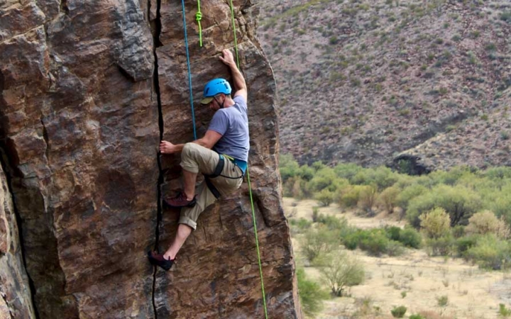 a person wearing rock climbing gear climbs a rock face in big bend texas